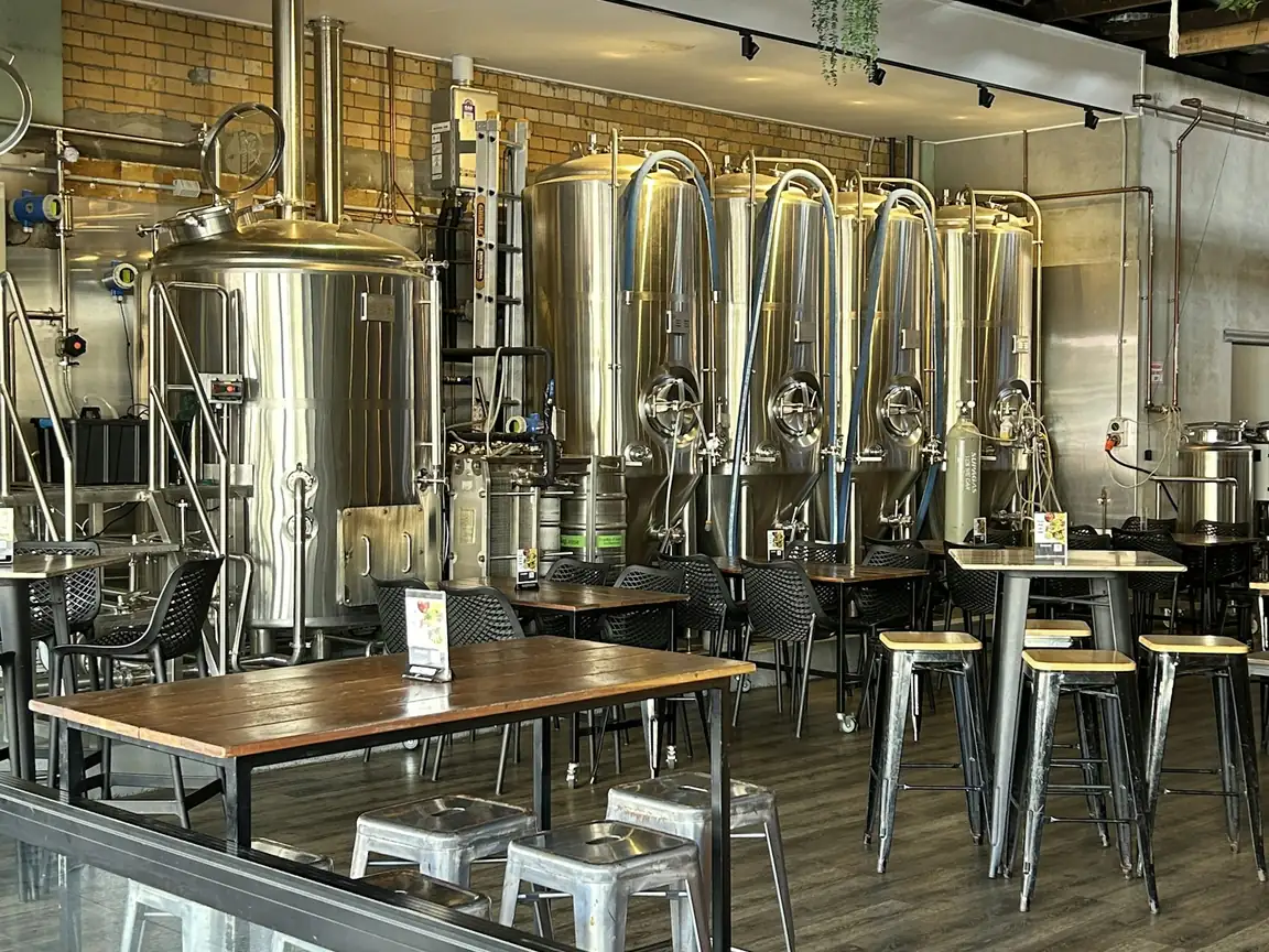 Copper brew kettle and steel fermenters with a sack of malt and a bowl of hops